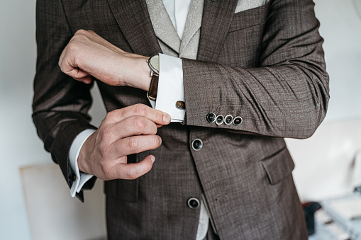 Man in a brown suit checking the cufflinks an his shirt
