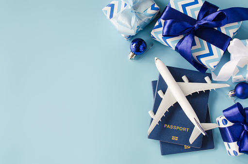 Travel present for Christmas or New Year. Toy airplane with passports and gift boxes on blue background. Top view or flat lay. Copy Space.