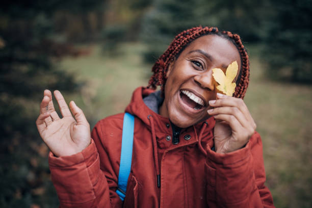 One woman, portrait of a black female hiker holding a yellow leaf in nature on autumn day alone.