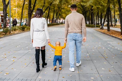 Young mother and father walking with their toddler in the park in autumn.