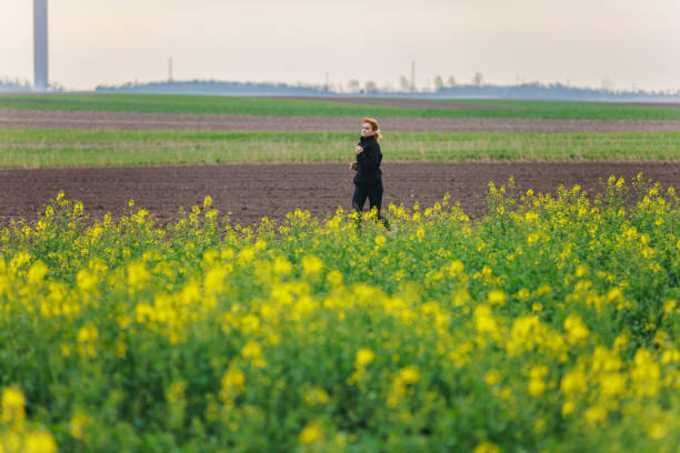 Mid adult woman running in the agricultural field by yellow flowering crops at dusk, active and healthy lifestyle