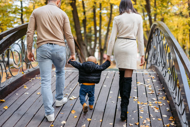 мама и папа гуляют со своим малышом по мосту в парке - couple autumn embracing bridge стоковые фото и изображения