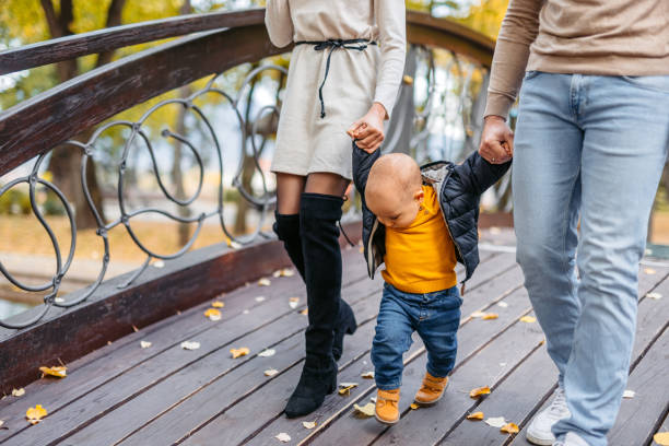 мама и папа гуляют со своим малышом по мосту в парке - couple autumn embracing bridge стоковые фото и изображения