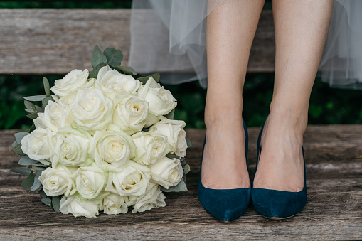 Bridal bouquet of white roses lies next to bride's feet with dark green shoes