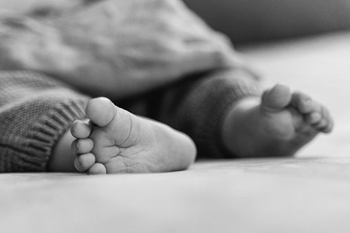 Newborn bliss: A heartwarming black and white photograph of tiny feet cradled in loving hands, symbolizing the purest form of love and protection.