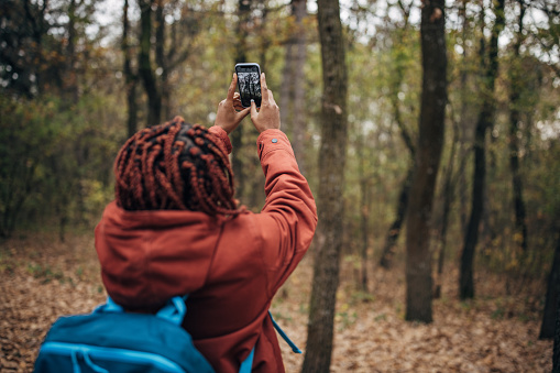 One woman, black female hiker using smart phone to take pictures in nature on autumn day alone.