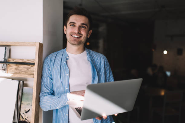 istock Cheerful man with laptop standing near wall 1444171262