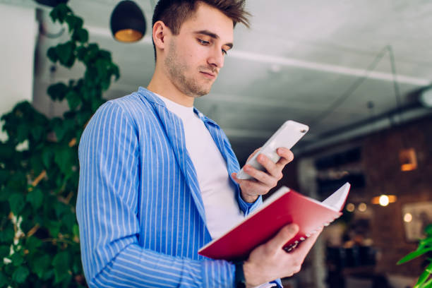 istock Intelligent Caucasian student making pictures of compendium text in education notepad for sending media file in message, male with smartphone device checking information on website while learning 1444171311