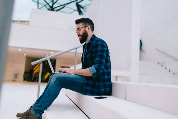istock Concentrated man with laptop sitting on stairs inside modern building 1444173008