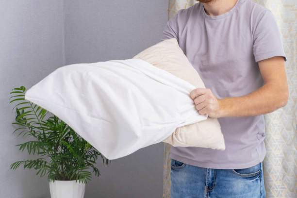 istock A man tucks a pillow with a fresh bright white pillowcase. Making the bed with fresh bed linen by white man. The day of the change of bed linen. The day of washing bed linen in the laundry room. 1444173036