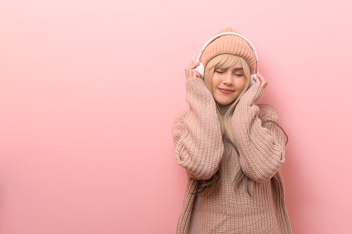 Portrait of Caucasian young woman wearing sweater using headphones  over pink  background