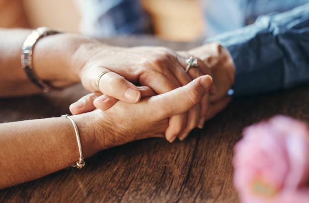 macro, casal e idosos de mãos dadas sobre a mesa para apoio, amor e cuidado em casa. zoom, sênior e mãos juntas para o vínculo, aniversário e romance no casamento, vida e aposentadoria - human hand old senior adult holding hands - fotografias e filmes do acervo