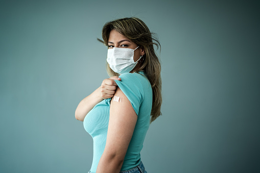Portrait of a young woman with a bandage on the arm and wearing a protective face mask