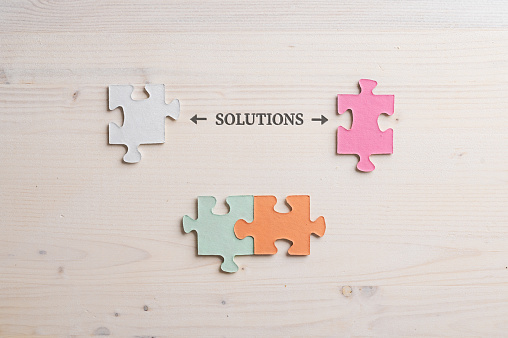 Conceptual image of problem solving with word Solution spelled over wooden background with four matching puzzle pieces around it.