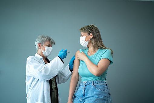 Doctor vaccinating a young woman - wearing a protective face mask