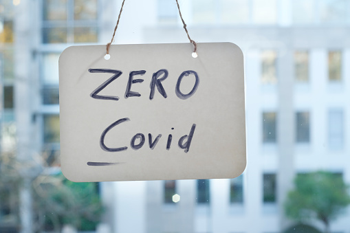 Zero covid sign on window, office buildings in the back