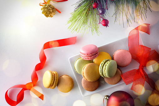 Stack of French macaroons of various flavors on ceramic plate with Christmas decoration on white table. Top view.
