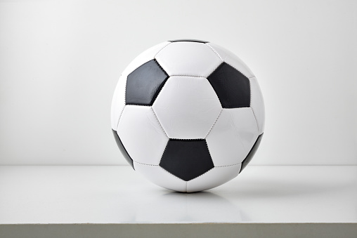 Detail view of classic black and white leather soccer ball isolated on table and light gray background. Front view.