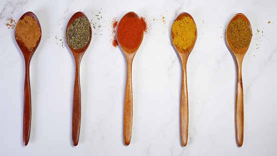5 dark wooden spoons with various spice powders on a light background