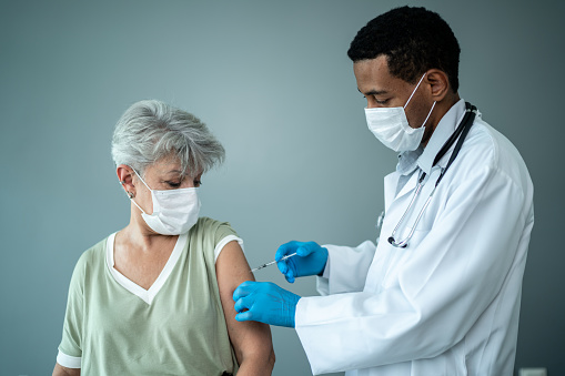 Doctor vaccinating a senior woman - wearing a protective face mask