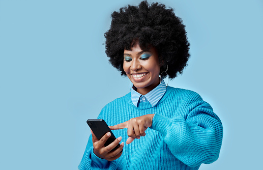 Happy, phone and black woman reading a blog on an internet website in a studio with mockup space. Happiness, smile and african girl networking on social media on as smartphone with a blue background.