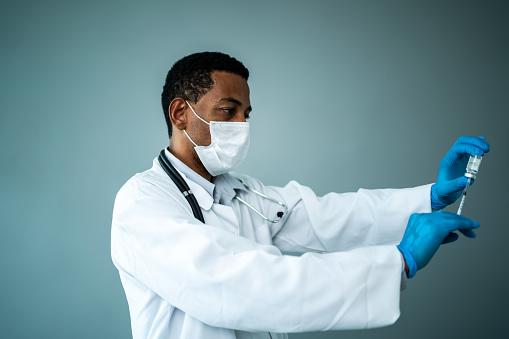 Doctor wearing a protective face mask and preparing injection on a studio shot