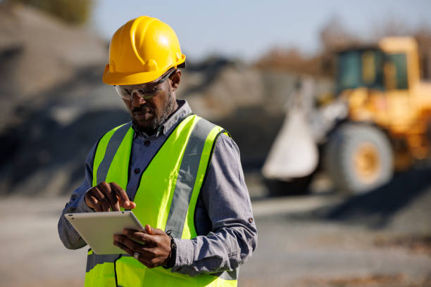 portrait of male engineer with hardhat using digital tablet while working at construction site - construction worker imagens e fotografias de stock