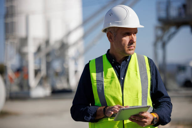 portret poważnego inżyniera w kapeluszu używającego tabletu cyfrowego podczas pracy w miejscu pracy - fuel storage tank industrial building construction development zdjęcia i obrazy z banku zdjęć