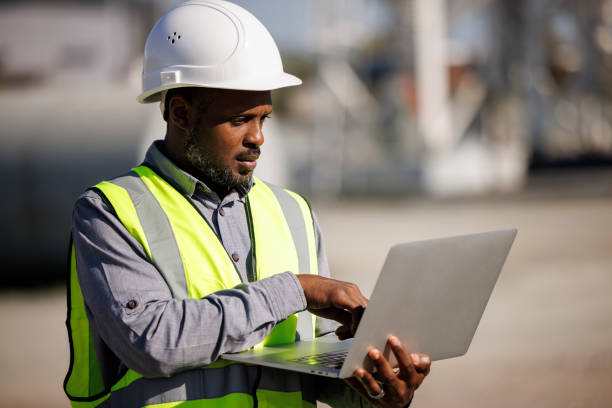 portret inżyniera w kapeluszu używającego laptopa podczas pracy w miejscu pracy - fuel storage tank industrial building construction development zdjęcia i obrazy z banku zdjęć