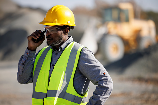 Portrait of  industry worker or engineer with hardhat and protective eyewear using walkie-talkie at construction site