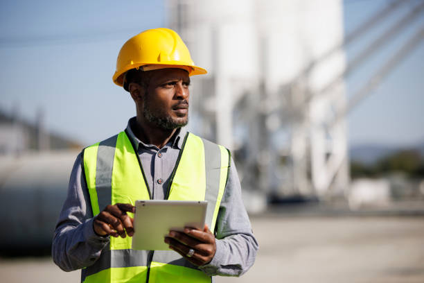 ritratto di ingegnere maschio con elmetto che utilizza tavoletta digitale mentre lavora sul suo cantiere - construction safety mid adult men road construction foto e immagini stock