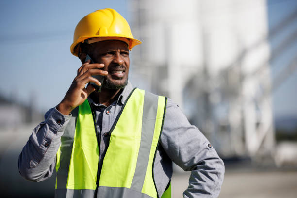 Worried male engineer with hardhat talking on mobile phone at industrial facility stock photo