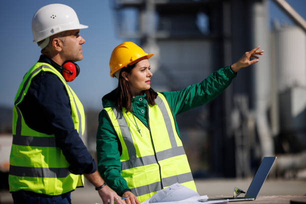 Male and female industrial engineers in hard hats discuss new project while using laptop stock photo