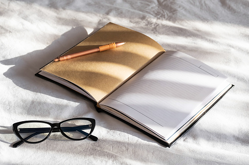 Mock up open notebook, pen and eyeglasses on white bedding.