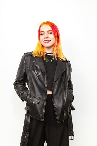 Studio portrait of an 18 year old white woman with brightly dyed hair in a black leather jacket against a white background