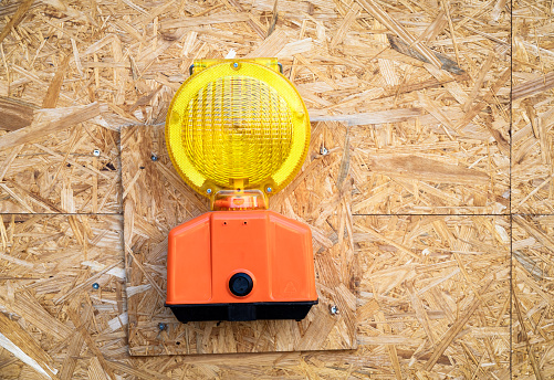 Close-up of a construction warning lantern on a site, against a wood chipboard barrier background.