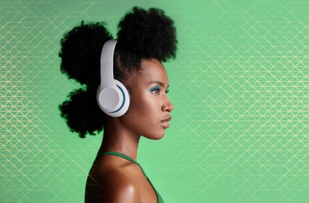 mulher negra, fones de ouvido de música e penteado de moda no fundo do estúdio com padrões geométricos verdes e cosméticos de maquiagem. estilo, tendência ou orgulho para modelo de beleza ouvindo podcast de rádio jamaicano - environmental conservation audio - fotografias e filmes do acervo