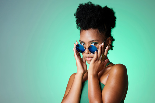 Portrait of black woman in green with sunglasses in the studio. Mockup for natural beauty, fashion and makeup in spring or summer. Black model in trendy glasses, modern and style on green background