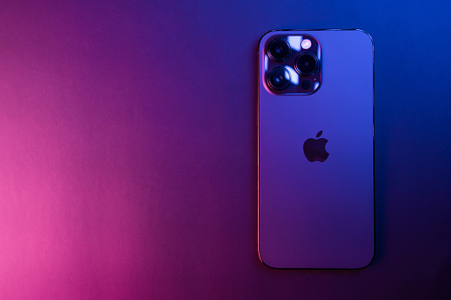 Closeup of iPhone 14 Pro Max Space Black isolated on black background illuminated by blue and pink lights. Low light. 3 featured cameras. Selective focus.
