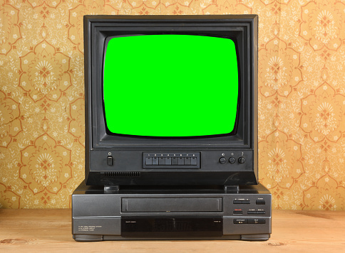Old black vintage TV with green screen and VCR on wallpaper background.