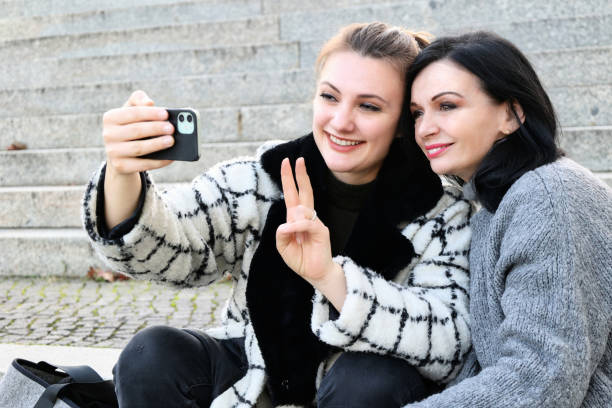 istock two women sitting outside on stairs and making a selfie 1444201583