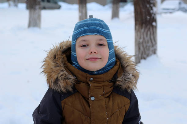 istock Portrait of an attractive boy outdoors in winter. He is wearing a warm hat and jacket, looking at the camera, and smiling. Against the background of snowdrifts and trees in the snow. 1444203473
