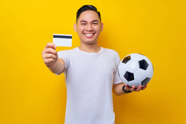 emocionado joven asiático fanático del fútbol con camiseta blanca sosteniendo un balón de fútbol y blanco en blanco aislado sobre fondo amarillo. concepto de estilo de vida de ocio deportivo de las personas - suit soccer men sport fotografías e imágenes de stock