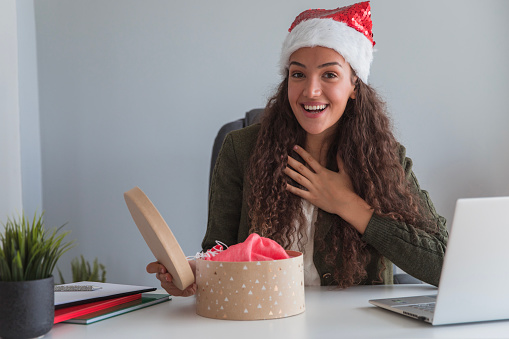 Happy young businesswoman wearing a Santa Claus hat and acting surprised upon opening a Christmas gift
