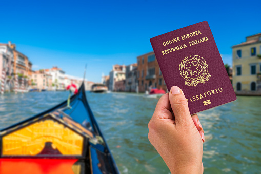 Close up view of woman's hand holding Italian passport in front of defocused Venice canal in Italy.