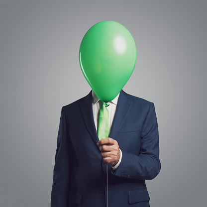 Anonymous corporate businessman hiding his head behind a green balloon