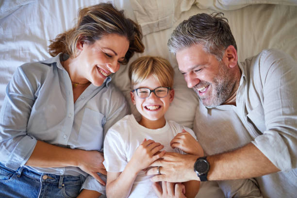 家族、くすぐり、幸せなお母さんとお父さんが笑い、家の寝室で楽しんでいるベッドに横たわる子供。オーストラリアの家でリラックスする男女の両親を持つ少年のポートレート - tickling ストックフォトと画像