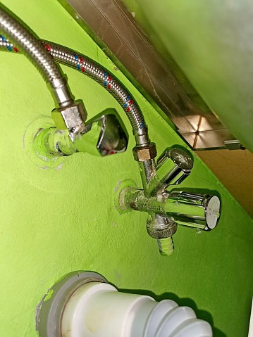 Plumbing valves under the kitchen counter, with hoses and waste pipe, image