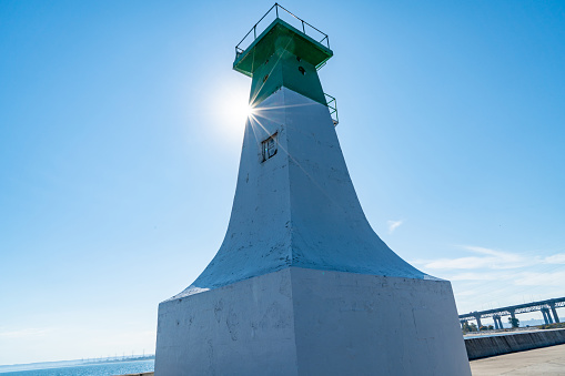 Lighthouse tower located behind rough mountainous coast of calm sea in sunny day