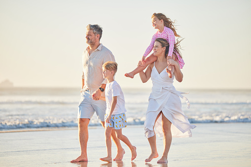 Family, beach and kids on the sand in nature for summer together spending quality time. Sea water, ocean waves and walking of a happy mother, man and children holding hands with happiness in the sun